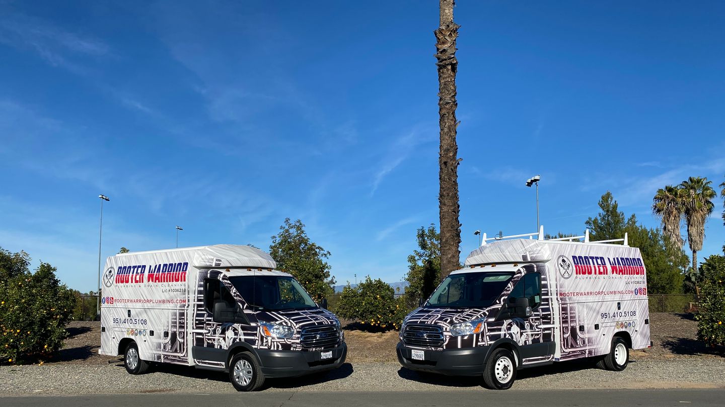Two Rooter Warrior Plumbing service trucks parked side by side under a clear Riverside sky